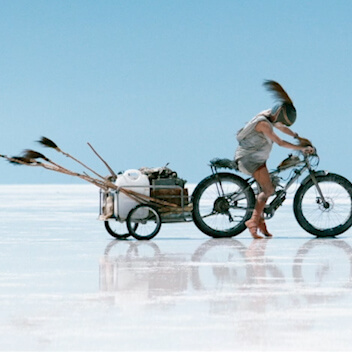 Film still from John Harvey's Canopy featuring a traveler on motor bike across salt plains